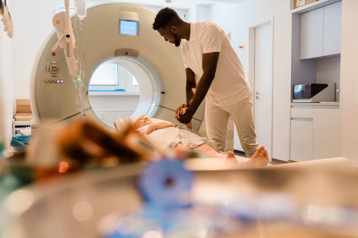 A technician comforting a patient by holding her hand after an MRI scan at a clinic.