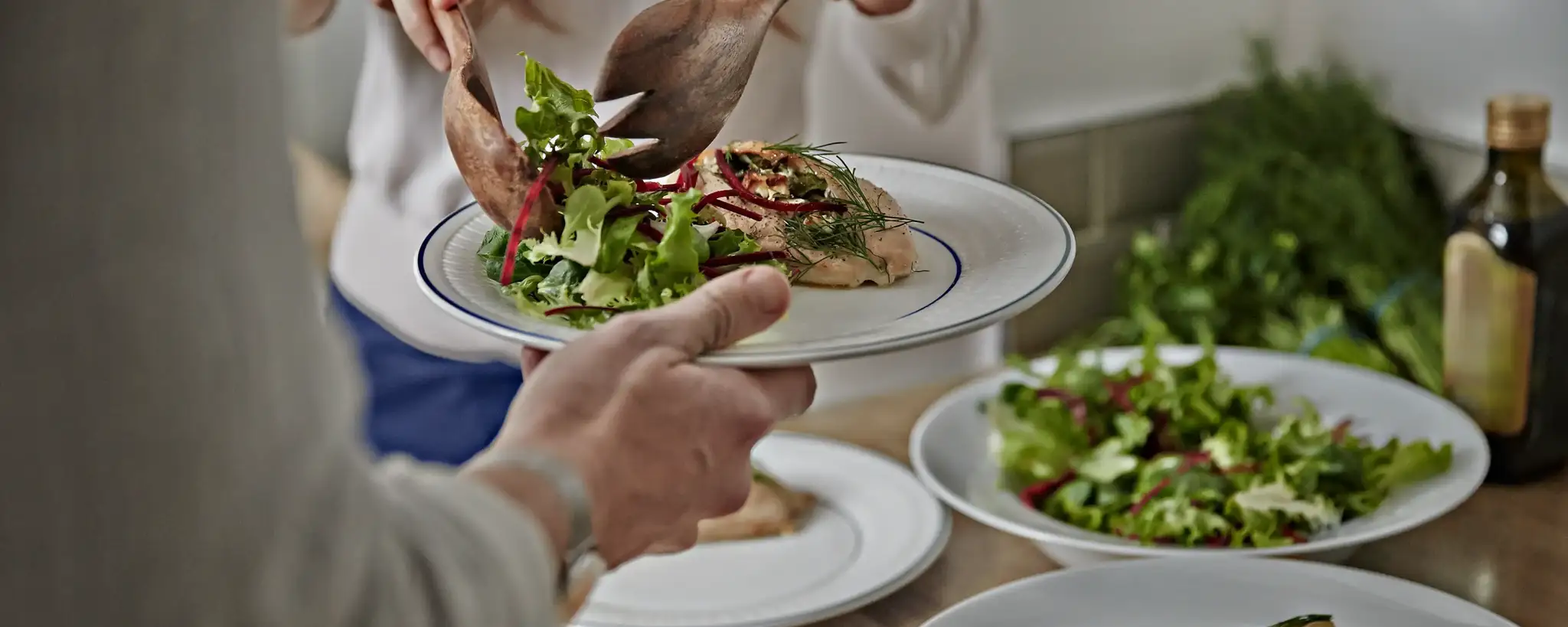 Person using utensils to put salad on a plate.