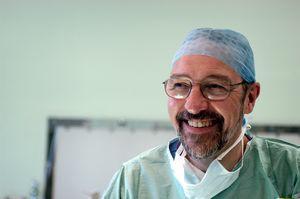 White male surgeon wearing glasses and wearing green surgical scrubs