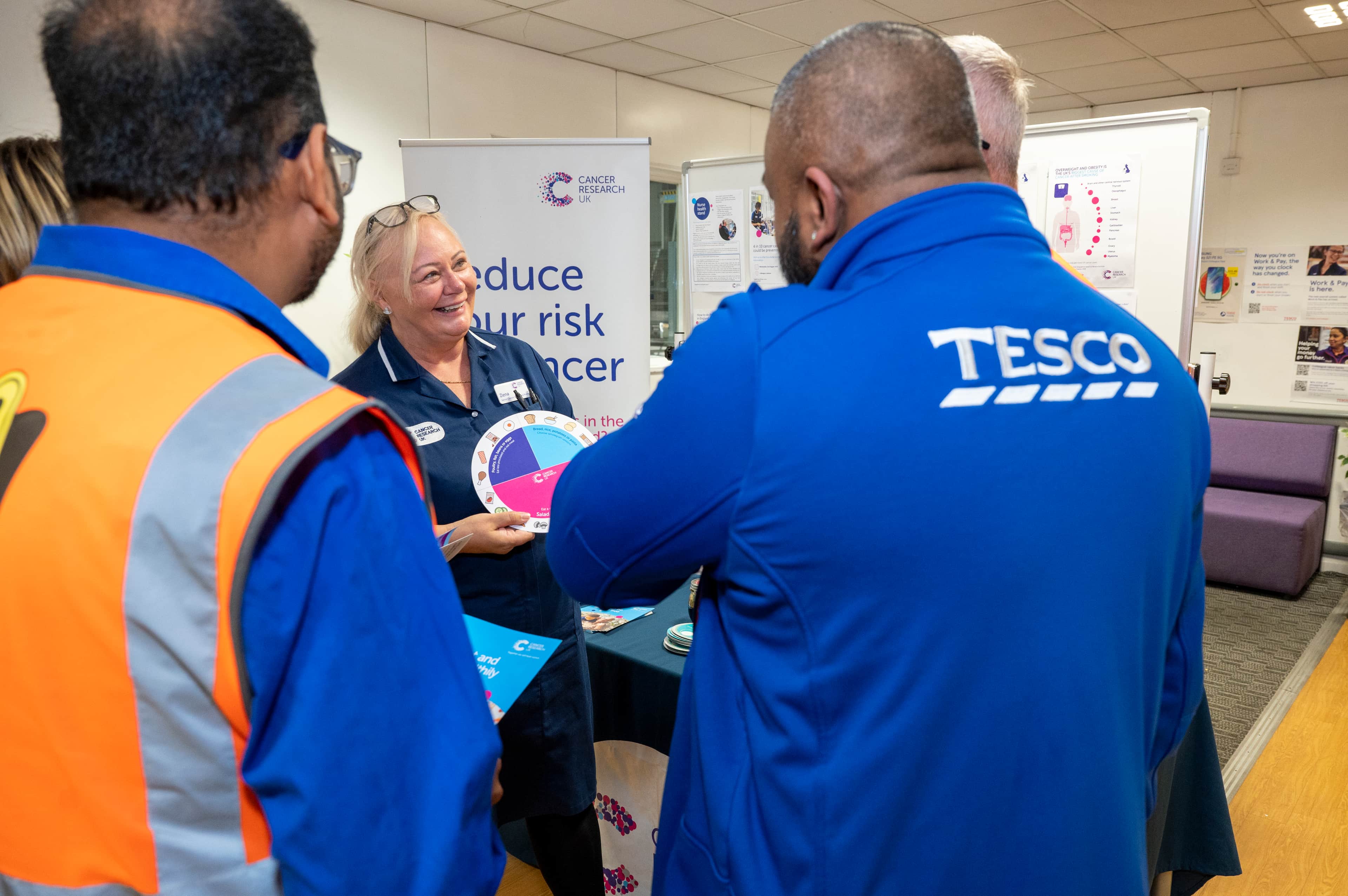 A Cancer Research UK nurse visits Tesco's Greenford distribution centre. She is smiling and talking to Tesco staff.