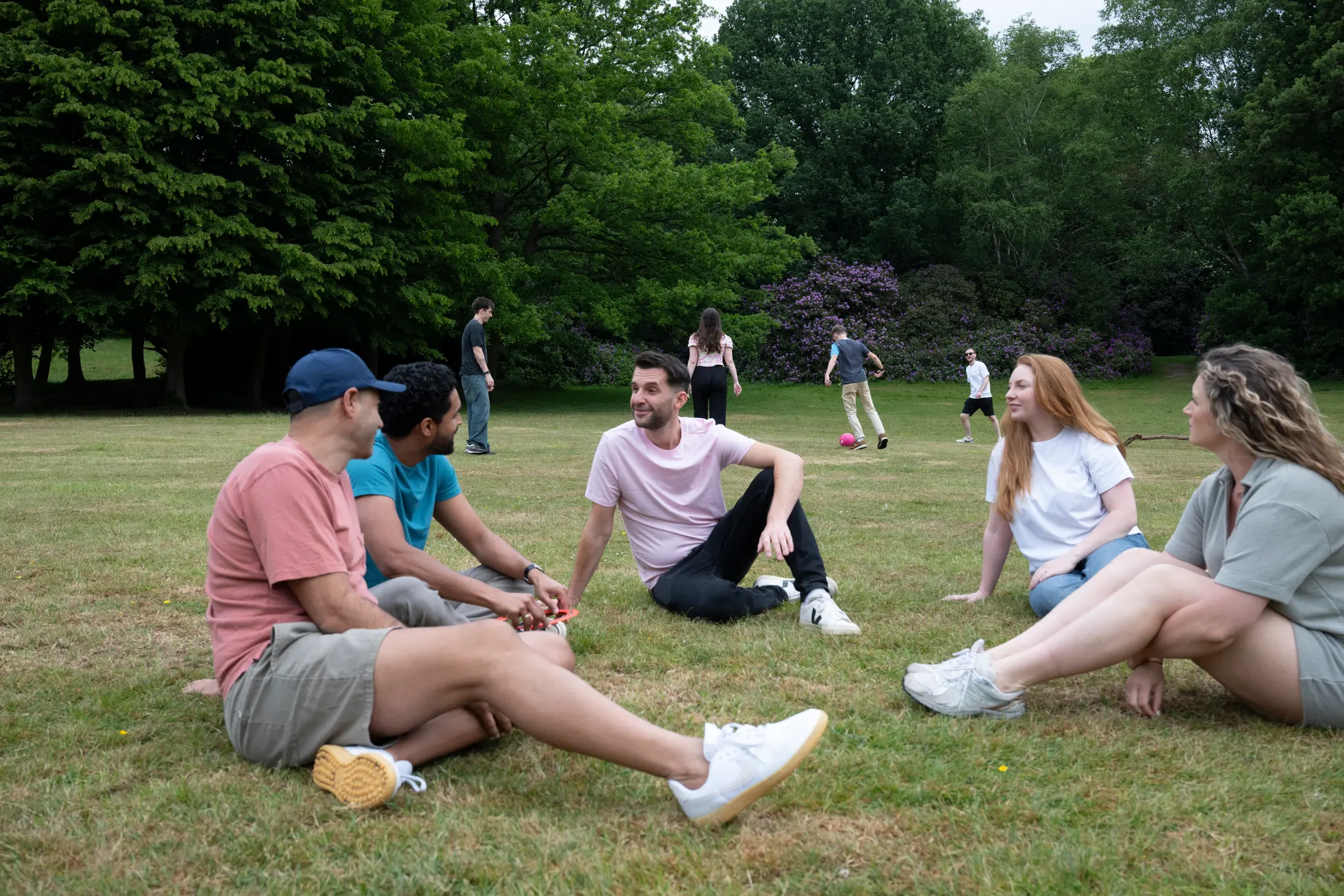 Photograph showing a group of people sitting in a park in a circle on theg grass.