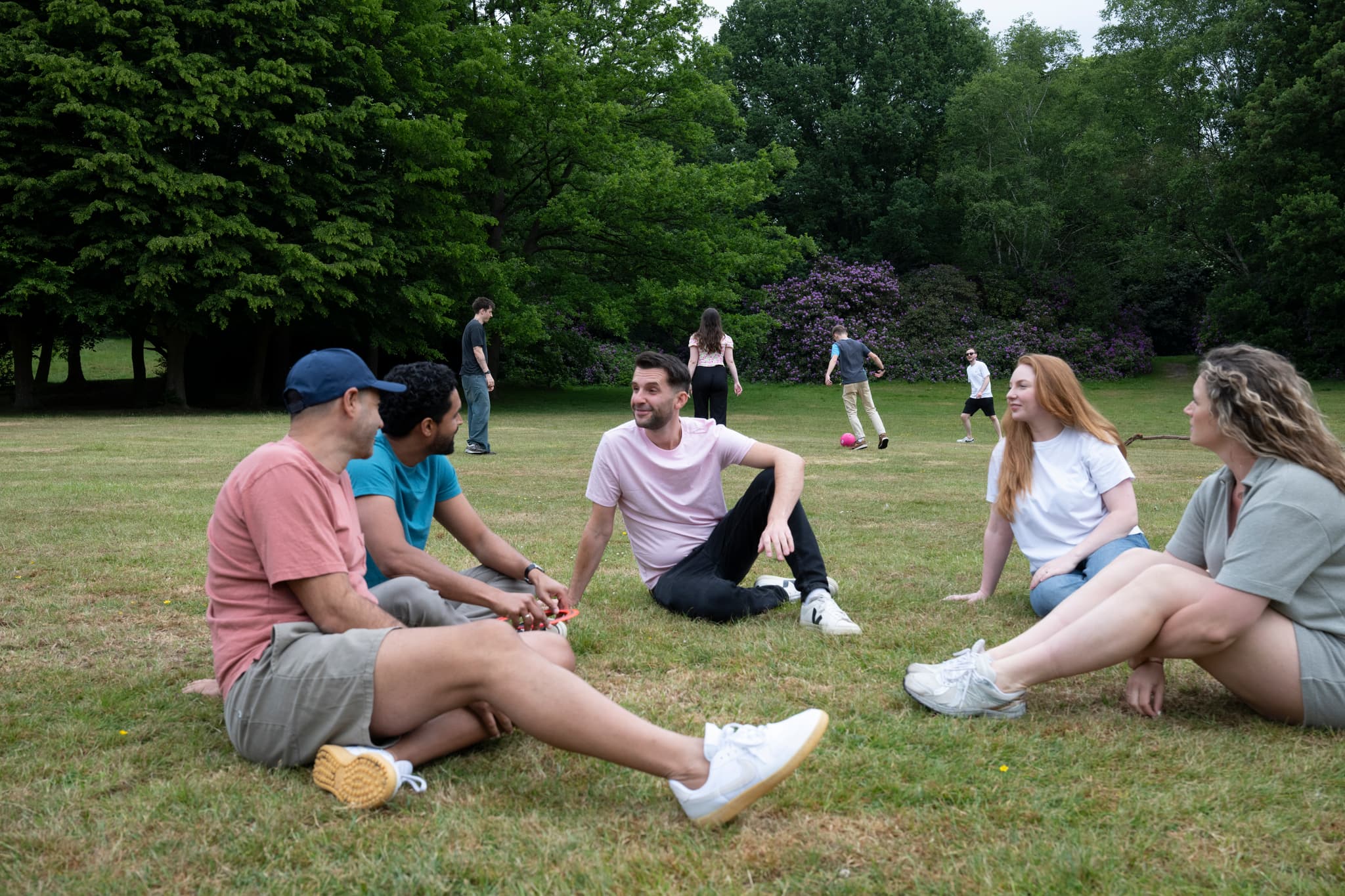 Photograph showing a group of people sitting in a park in a circle on theg grass.