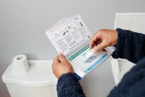 Photo showing a man in a bathroom opening a bowel cancer screening test kit from NHS England.