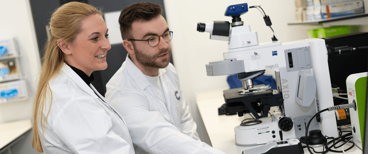 Two researchers looking at a microscope at a desk.