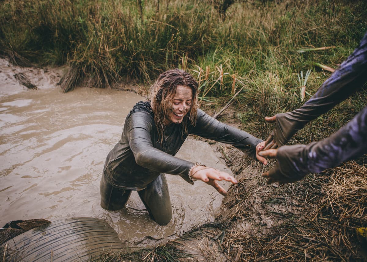 Woman covered in mud leaving a mud puddle and smiling during the CRUK Tough Mudder event.