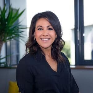 A smiling, smartly dressed woman in an office setting.