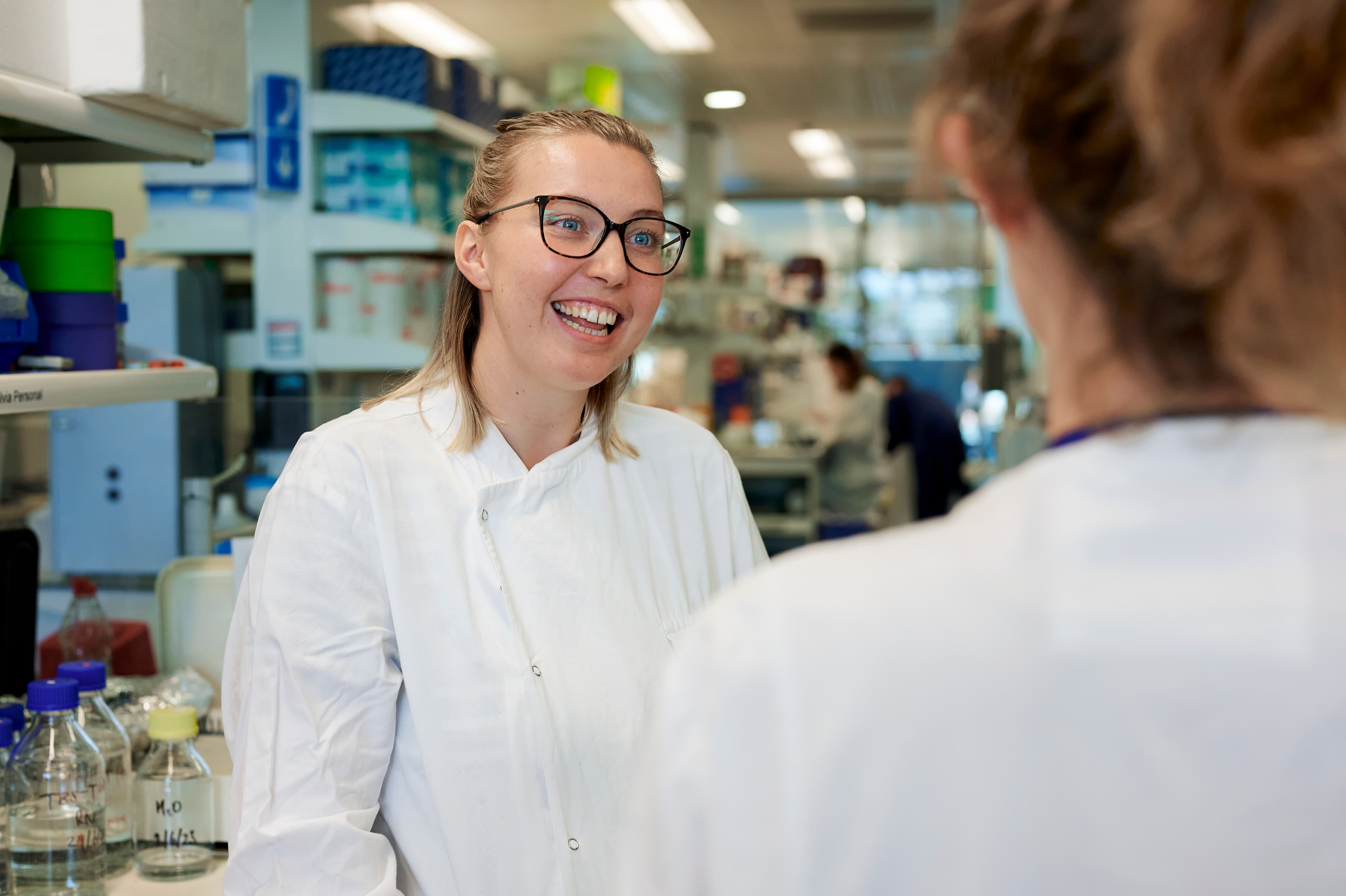 Photo of Hannah who is a researcher for Cancer Research UK talking to her colleague, Jessica. They're in happy conversation.