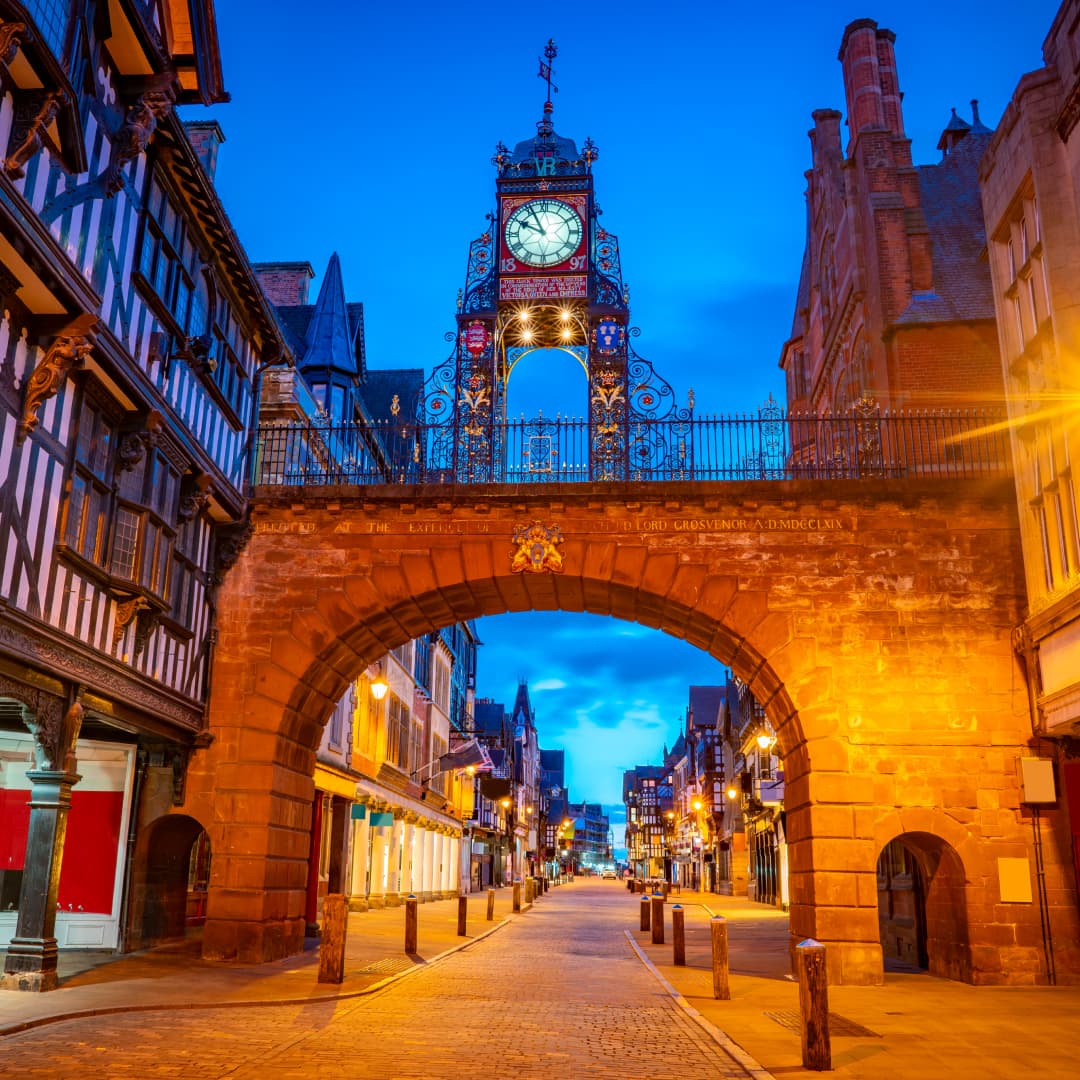 Photograph of a cobbled street and clocktower in Chester at night.