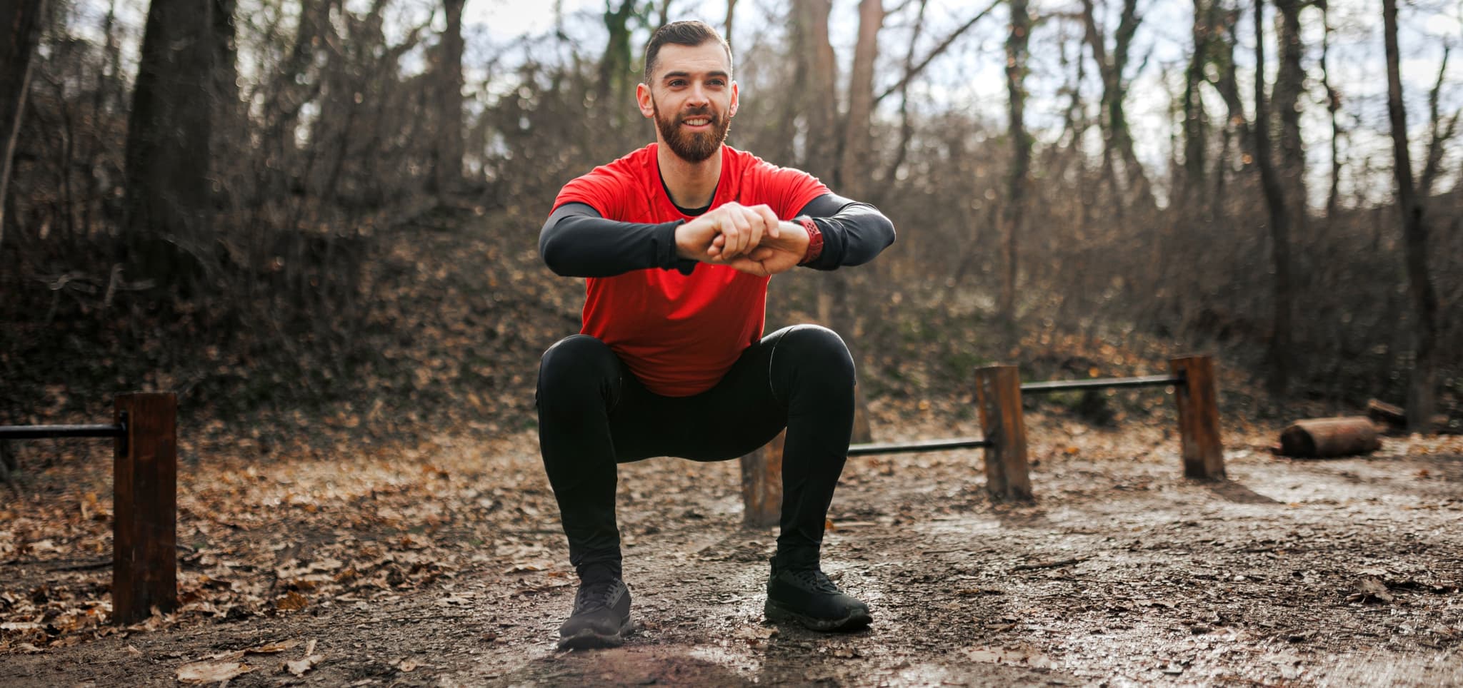 man doing a squat outdoors smiling.