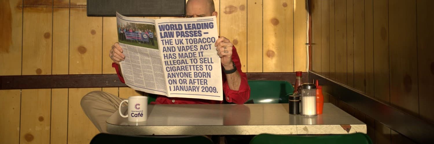 A man holding a newspaper with a headline about the Tobacco and Vapes Act.