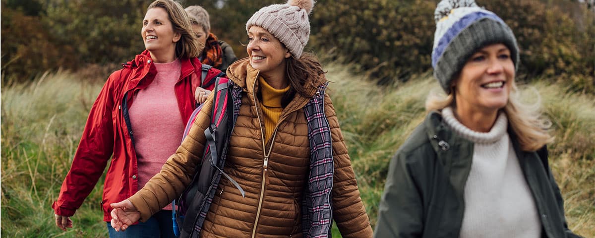 Image of three women walking together in a field wearing winter clothing.