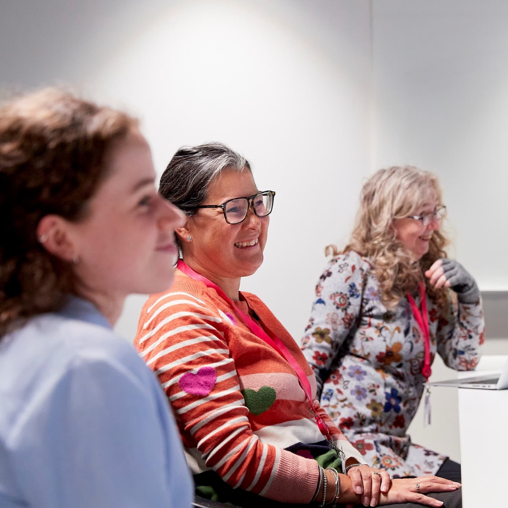 Three people sat at a table in a meeting. They are all smiling.