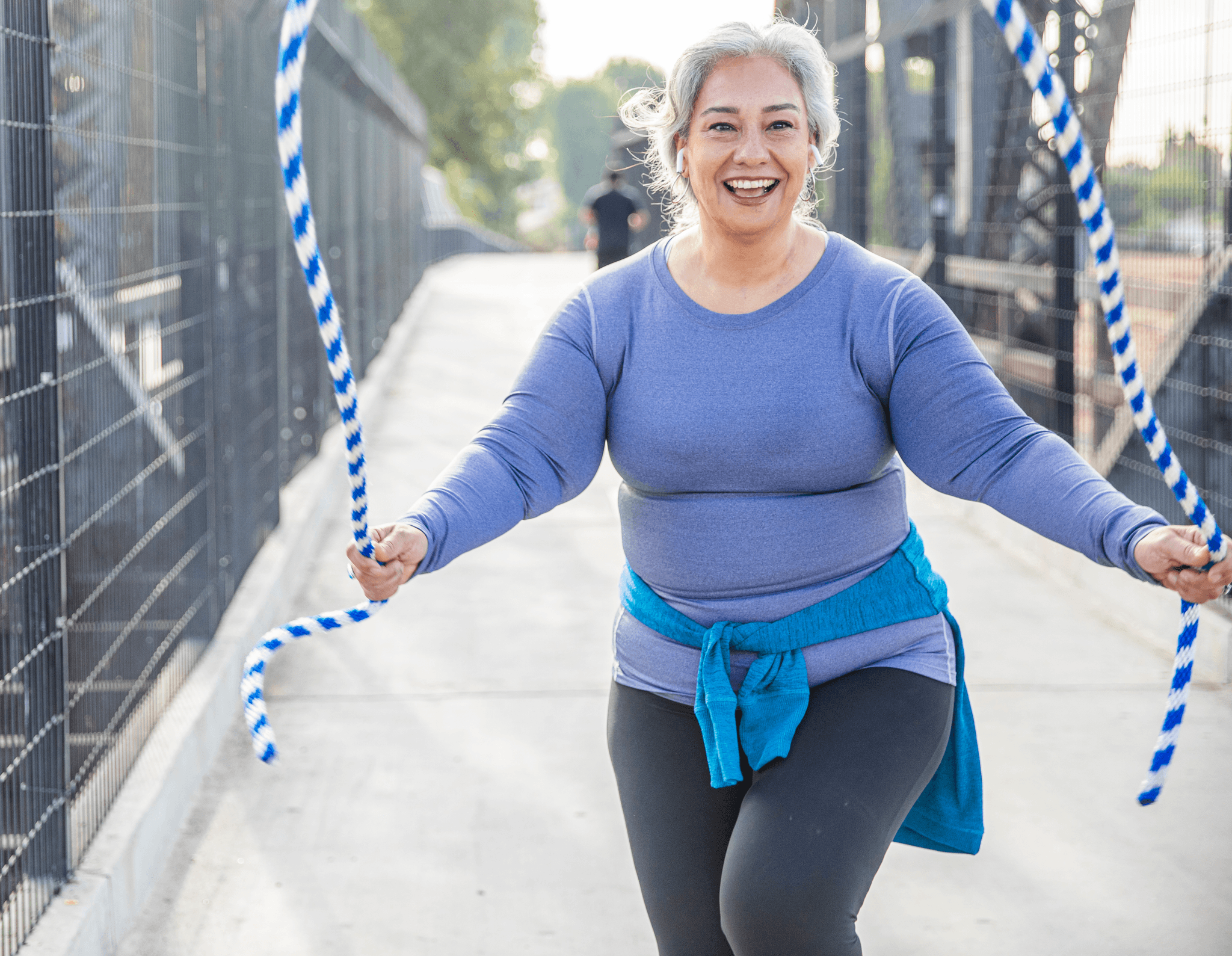 A photo of a smiling woman outdoors skipping whilst listening to music.