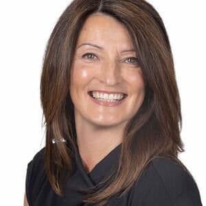 A smartly dressed woman with long brown hair smiling.