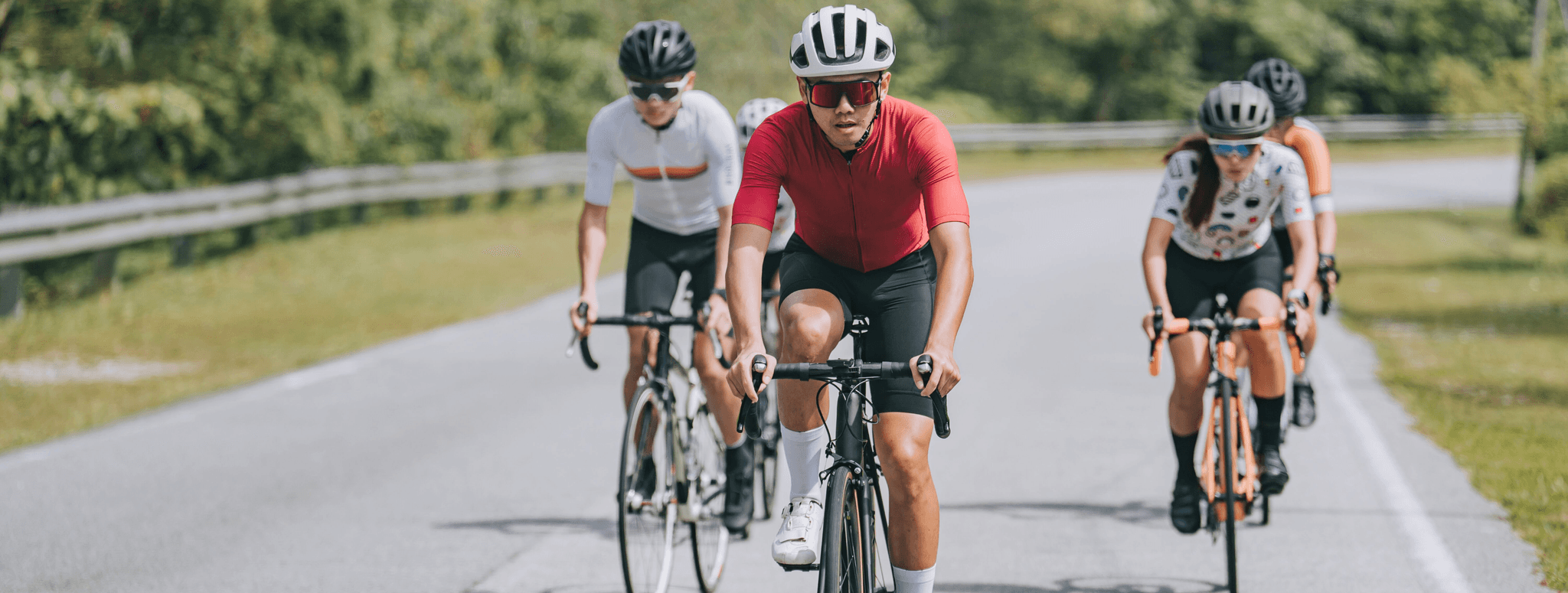 A photo of four cyclists wearing helmets, riding on an empty road.