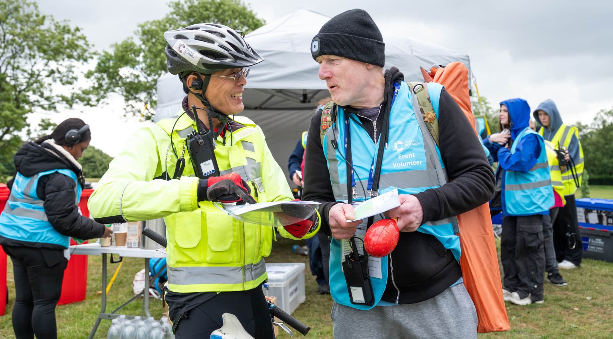 Image shows two male event volunteers, stood outside a marquee holding some instructions and chatting.
