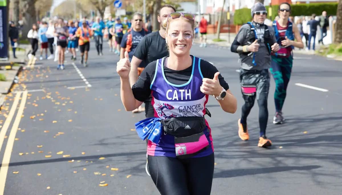 Woman wearing a CRUK T-shirt running and smiling during the Brighton marathon.