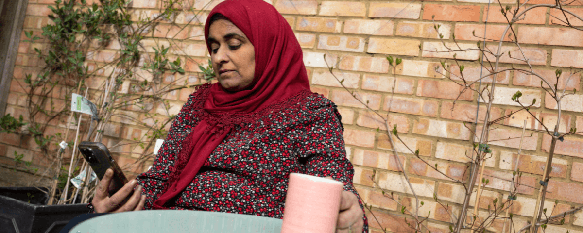 A woman is sat outside with a coffee reading information on their phone.