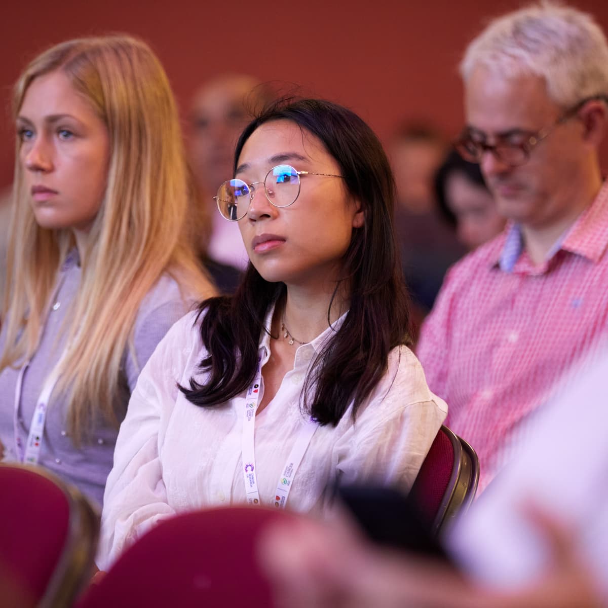 Three researchers sat in the audience of a conference, listening intently to the speaker.