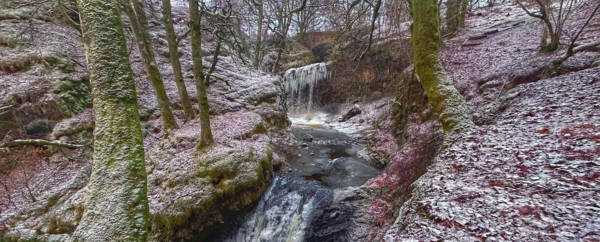 Small waterfall flowing through a rocky, snow-dusted forest.