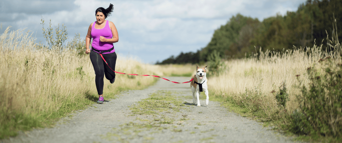 A woman jogging with her dog along a grassy countryside.