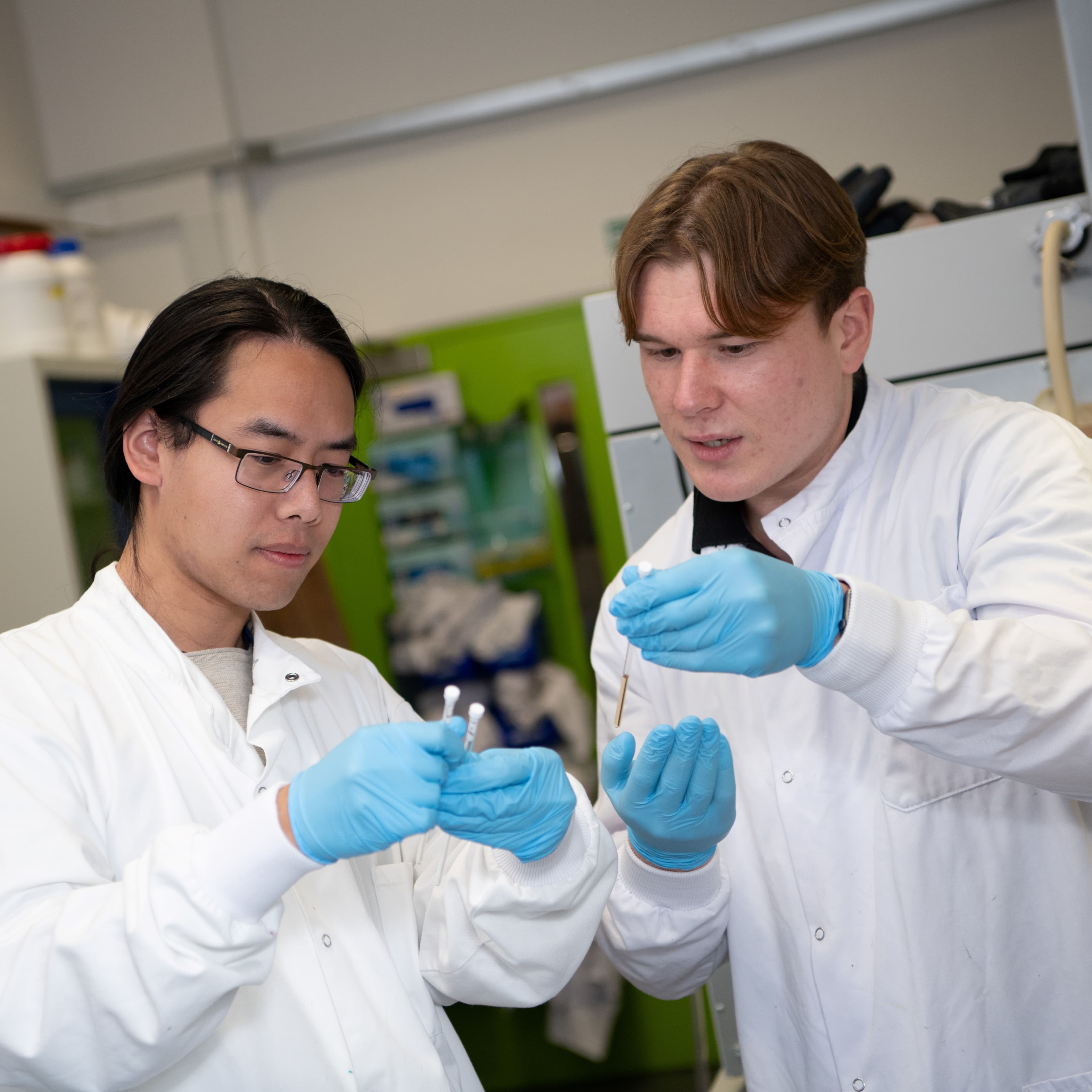 Two researchers in a lab looking at lab equipment and holding it in the air.