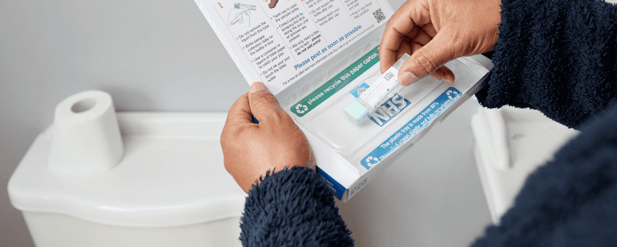 The photo shows a man in a bathroom opening a bowel cancer screening test kit from NHS England.
