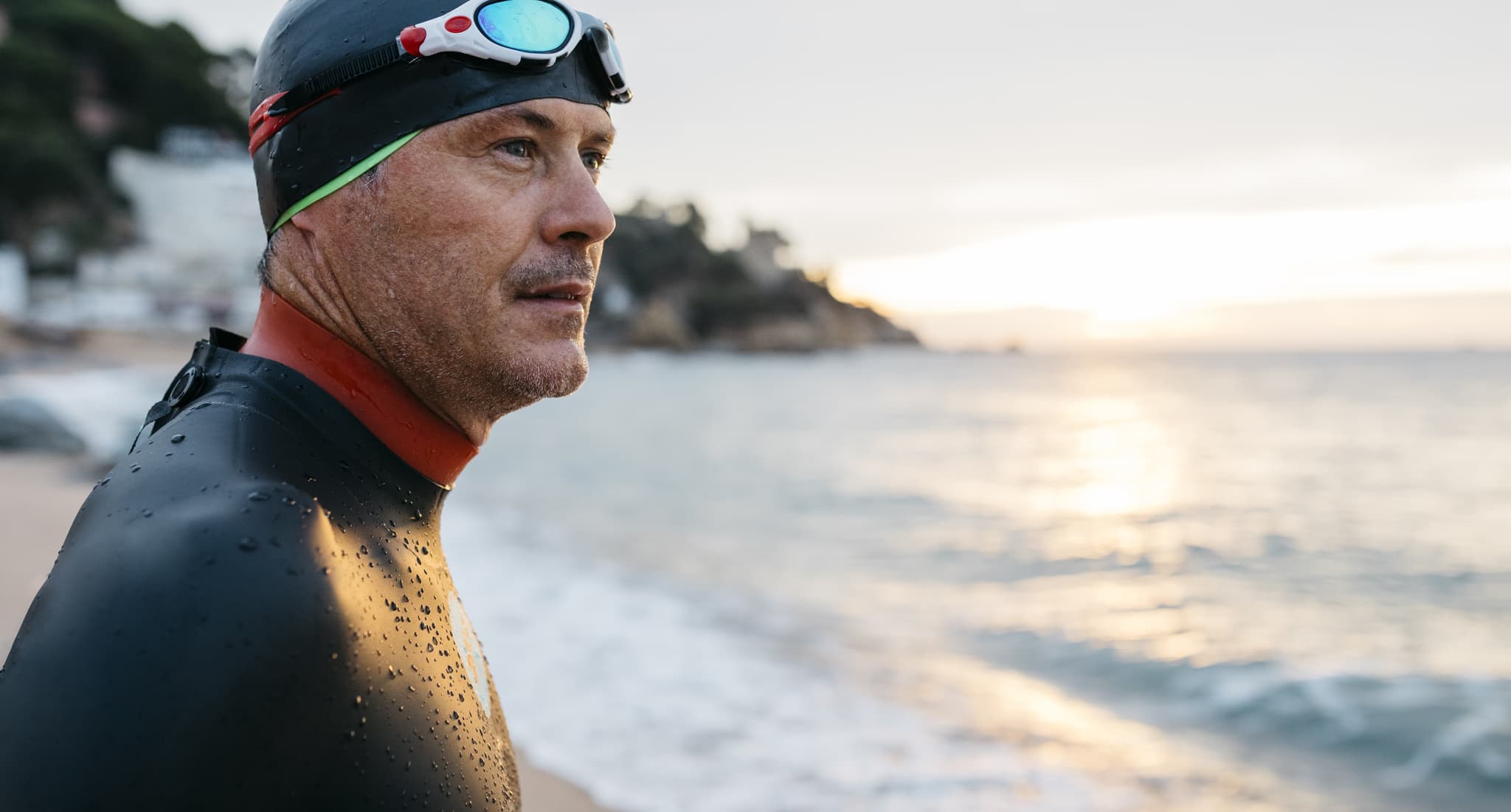 Close-up side shot of a man wearing goggles and swimming hat by the sea.