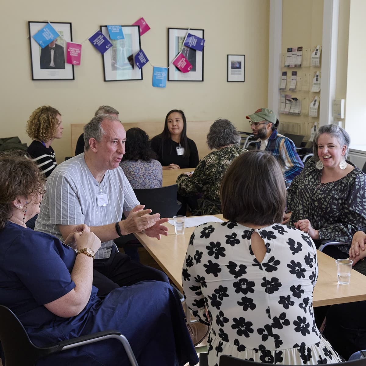 A group of people in a room. They are sat at tables having a discussion.