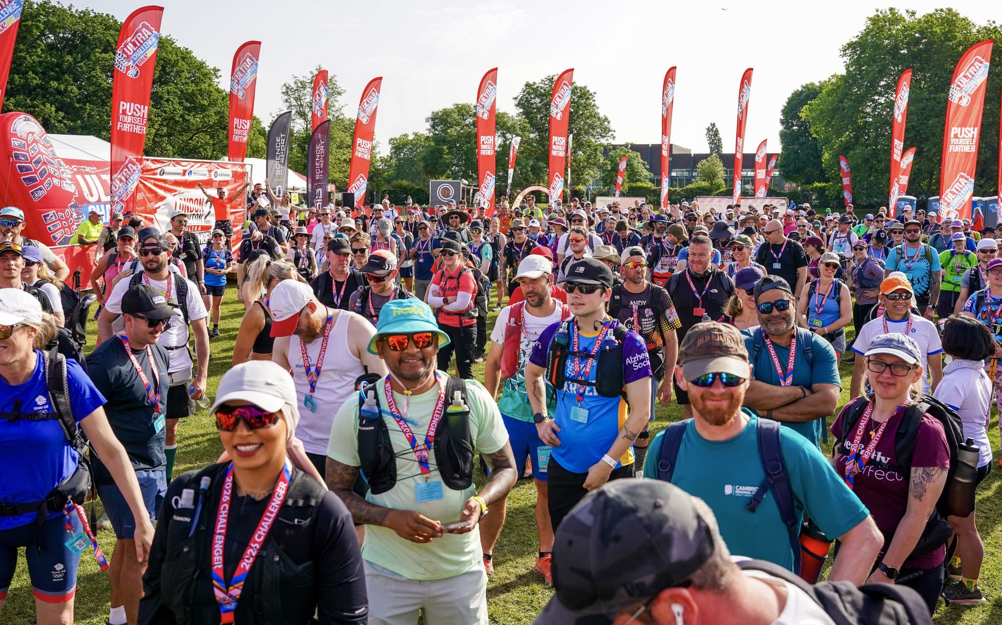 Large group of participants gathered at a sunny startline with flags in the background.