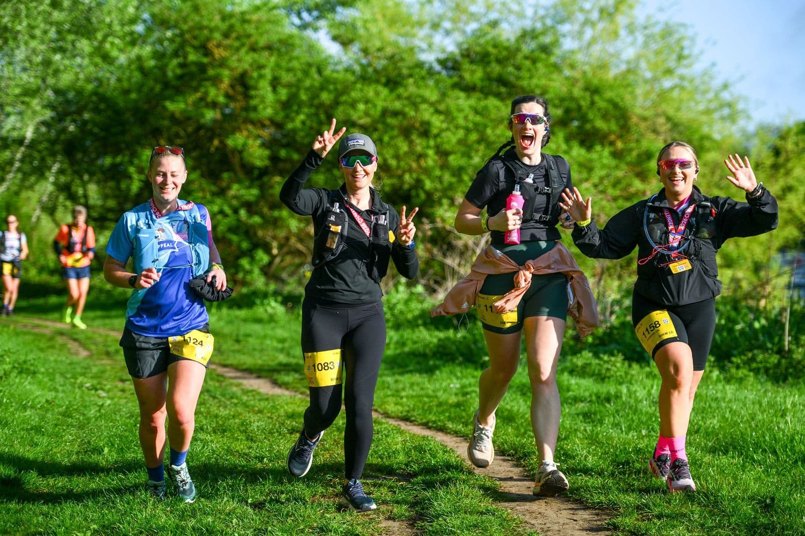 4 women runners in forefront with 2 at the back running through a field surrounded by trees.