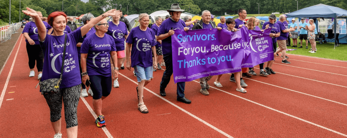 Group of Relay For Life participants walking on the track holding a banner.