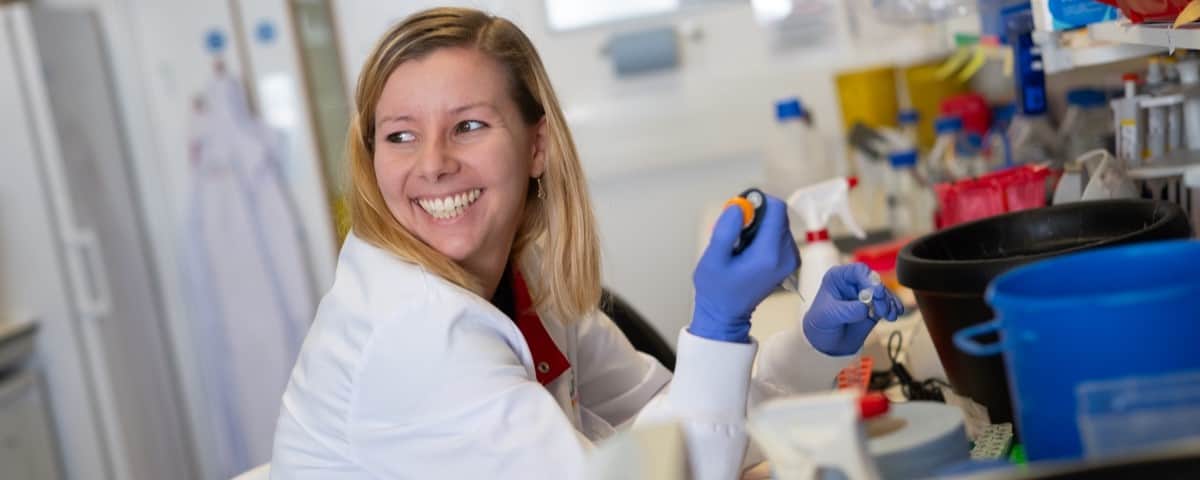 Researcher pipetting whilst sat at a lab bench and smiling.