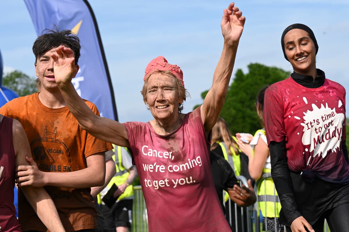 An elderly woman covered in mud celebrating during the CRUK Tough Mudder event.