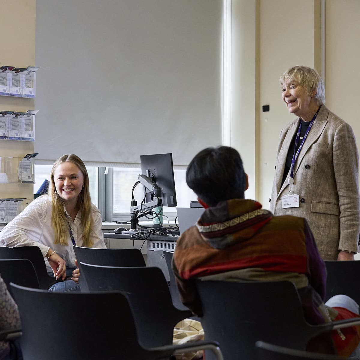 A group of people in a meeting. There is one person standing at the front of the room.