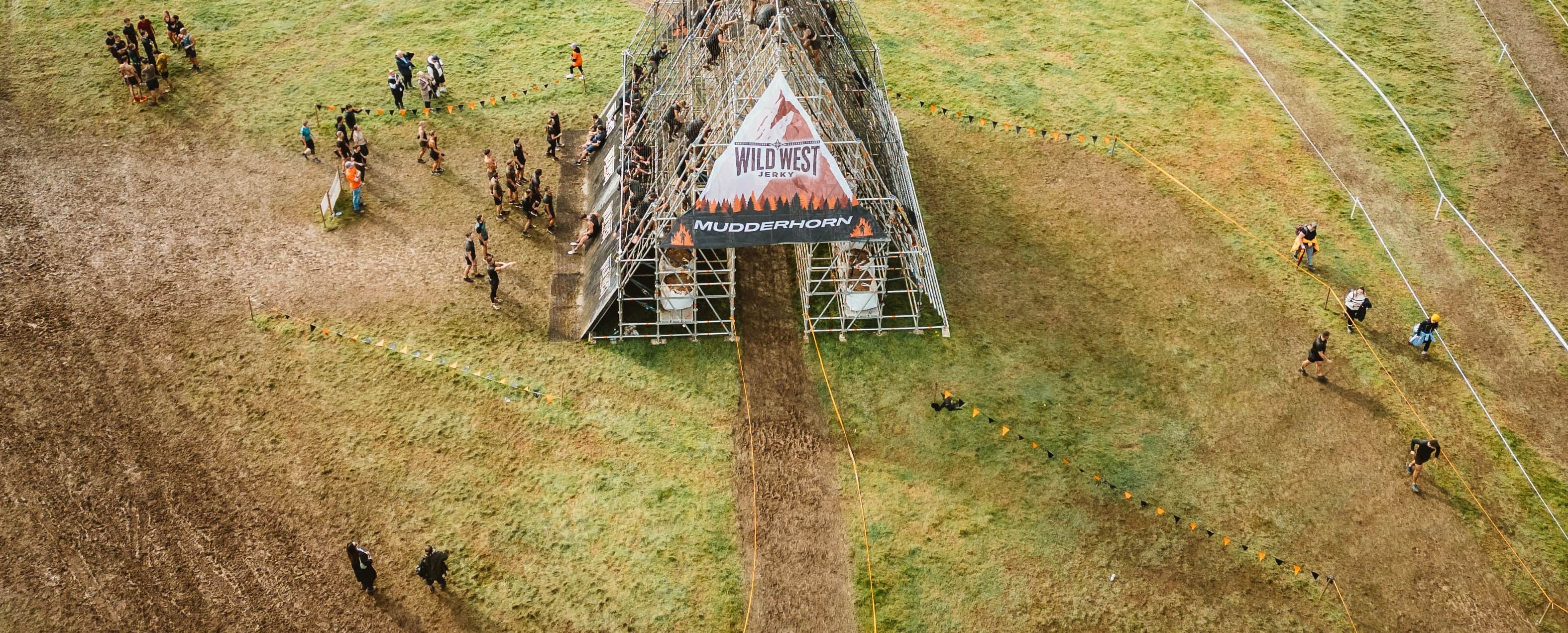people in the middle of a green field climbing up and going down a metal house shaped structure.