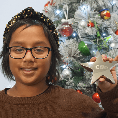 A photo of Zara standing in front of a Christmas tree, holding a Star Award.