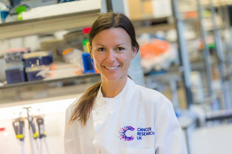 Researcher standing in a lab coat smiling.