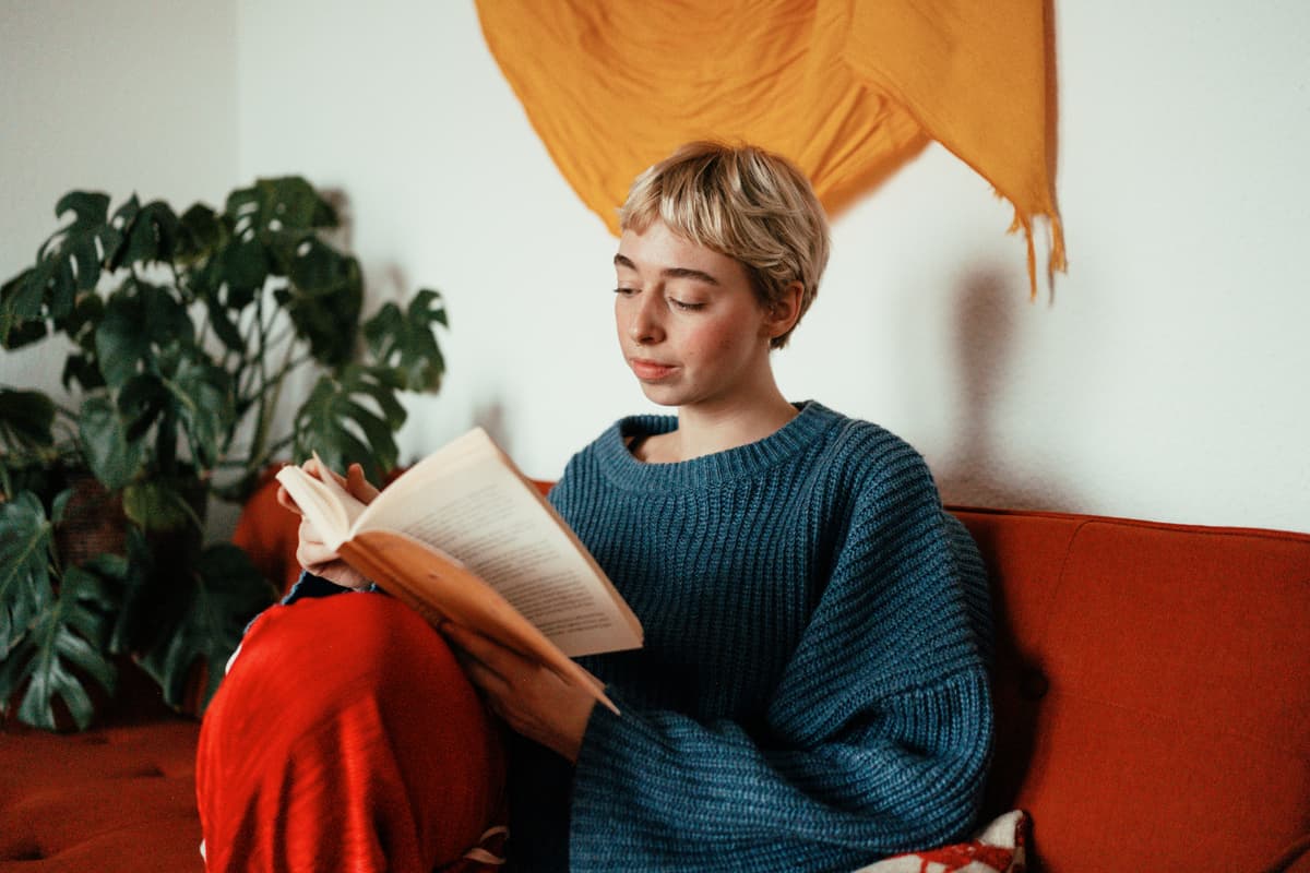 Woman sat on sofa reading a book.