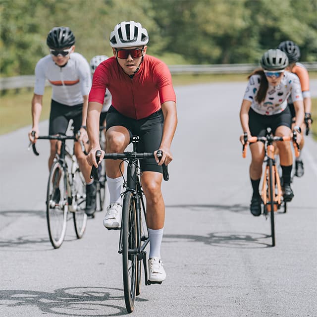 A photo of several cyclists riding together in a group on an empty road.