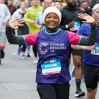 A runner in Cancer Research UK outfit and a winter hat with her arms up taking part in a race.