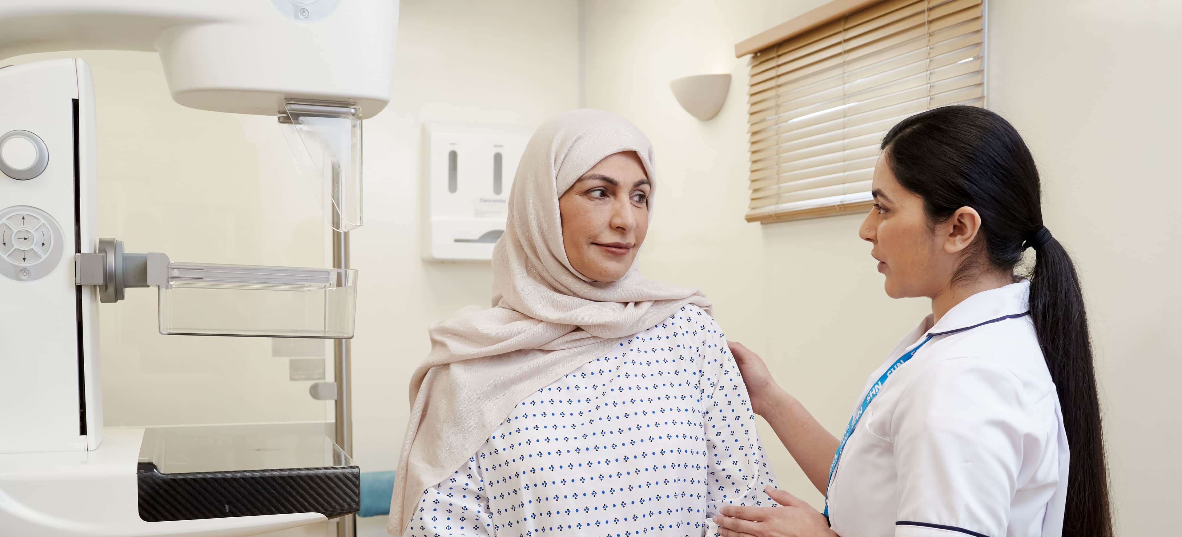 A photo of a mammographer with a patient, wearing a hospital gown, before a mammogram.
