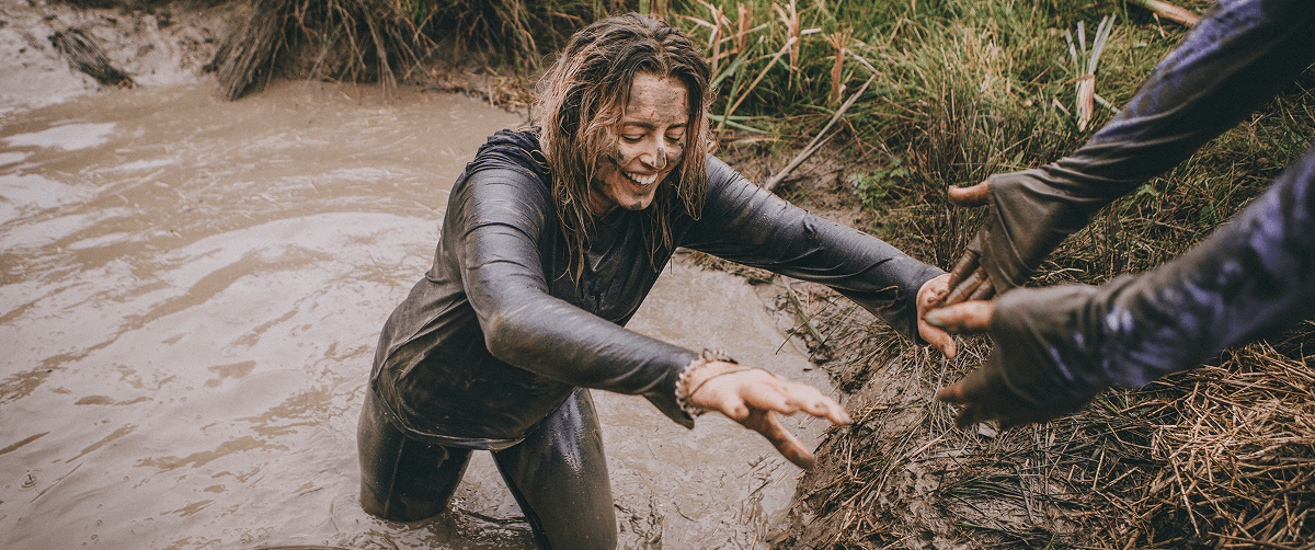 Woman covered in mud leaving a mud puddle and smiling during the CRUK Tough Mudder event.