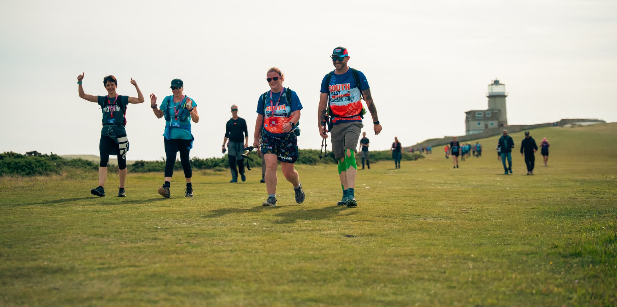 Group of walkers on the south coast with a lighthouse in the background.