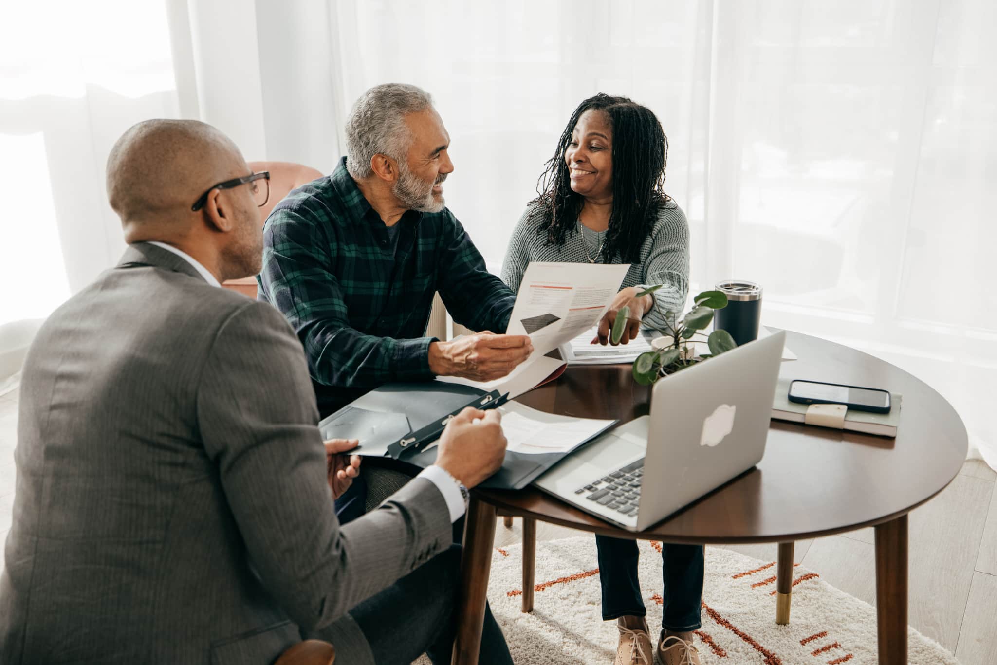 A legal professional sat around a table with two clients. They are looking at documents together and smiling.