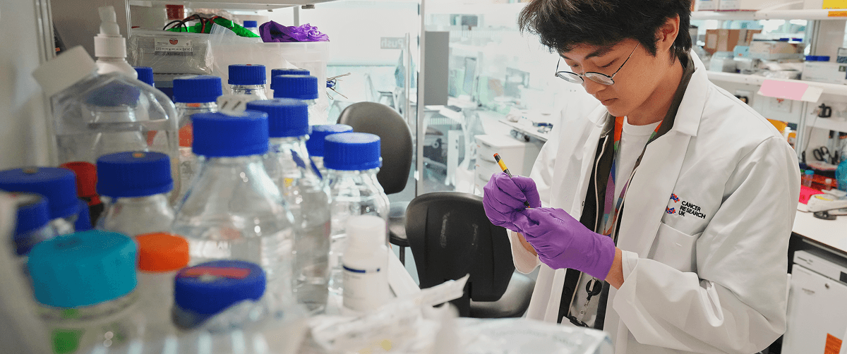 Researcher in a lab, in the forefront of the image are a number of bottles and containers.