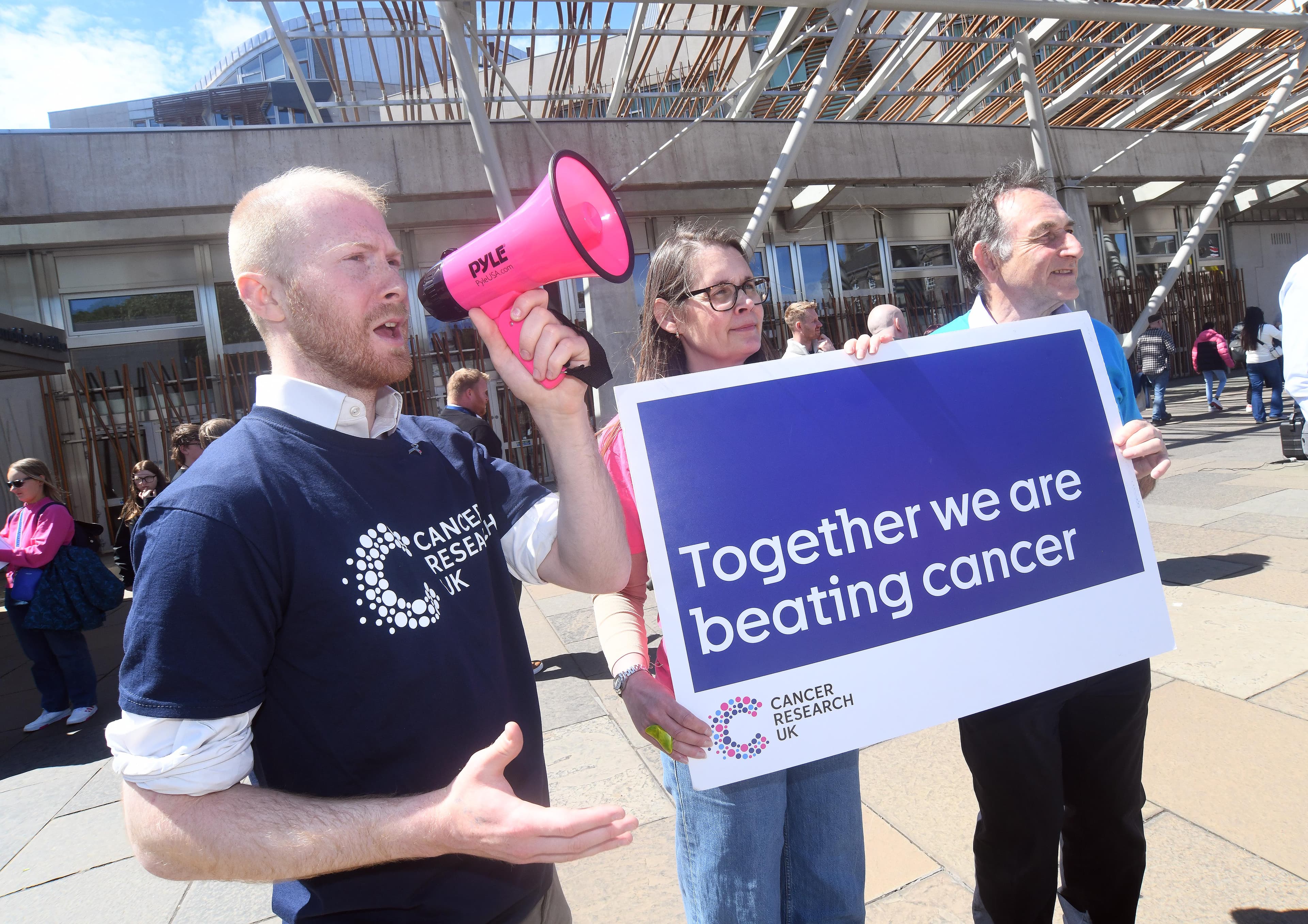 A photo of three Campaigns Ambassadors holding a megaphone and a sign that reads Together we are beating cancer.