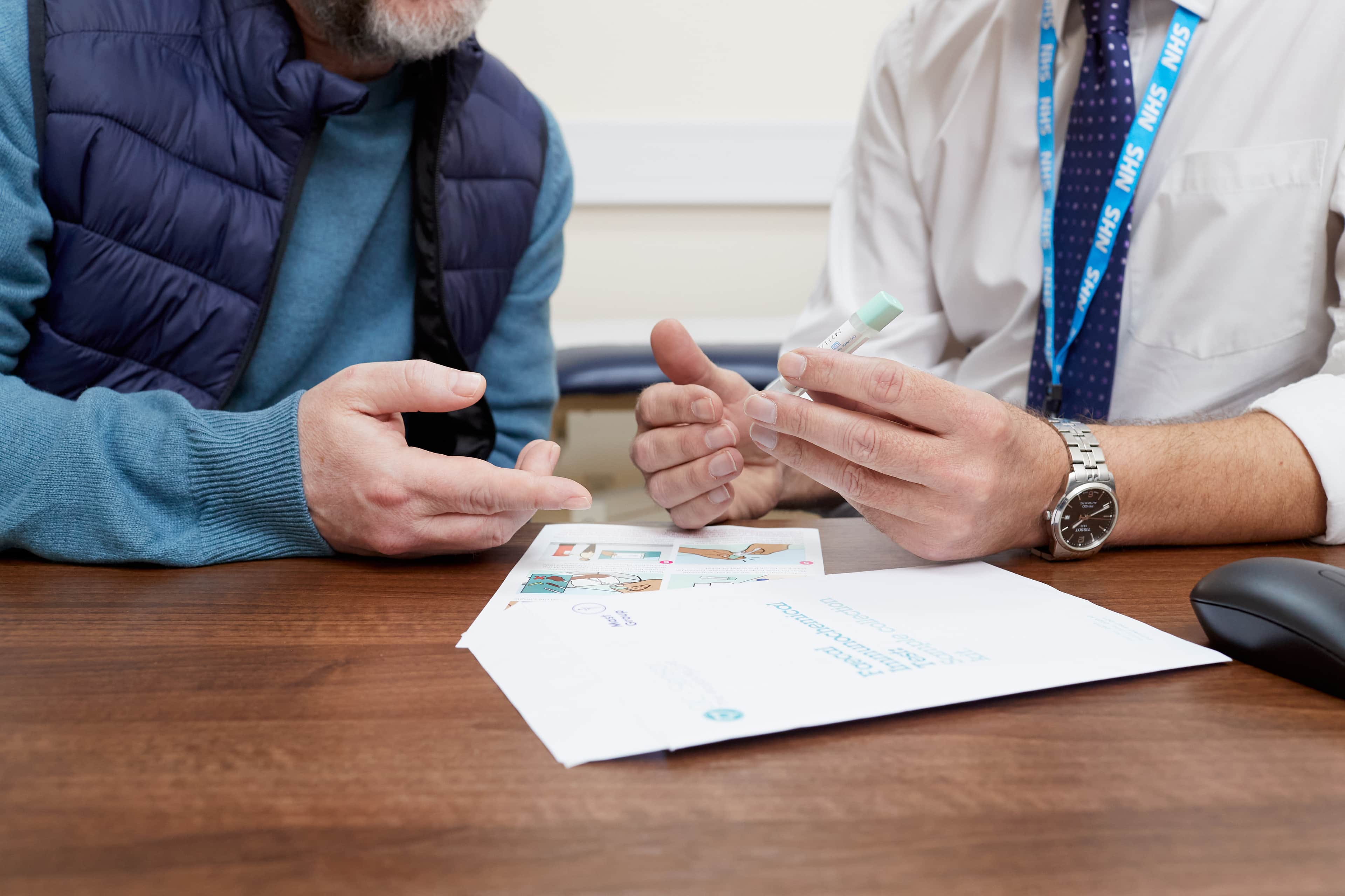 This photo shows a GP talking to a patient about a symptomatic Faecal Imunochemical Test (FIT) kit from England.