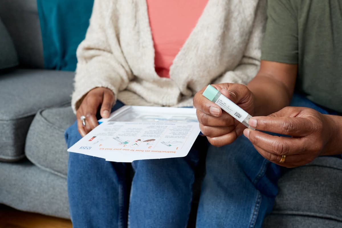 Two people sitting next to each other on a sofa, holding a bowel screening test kit.