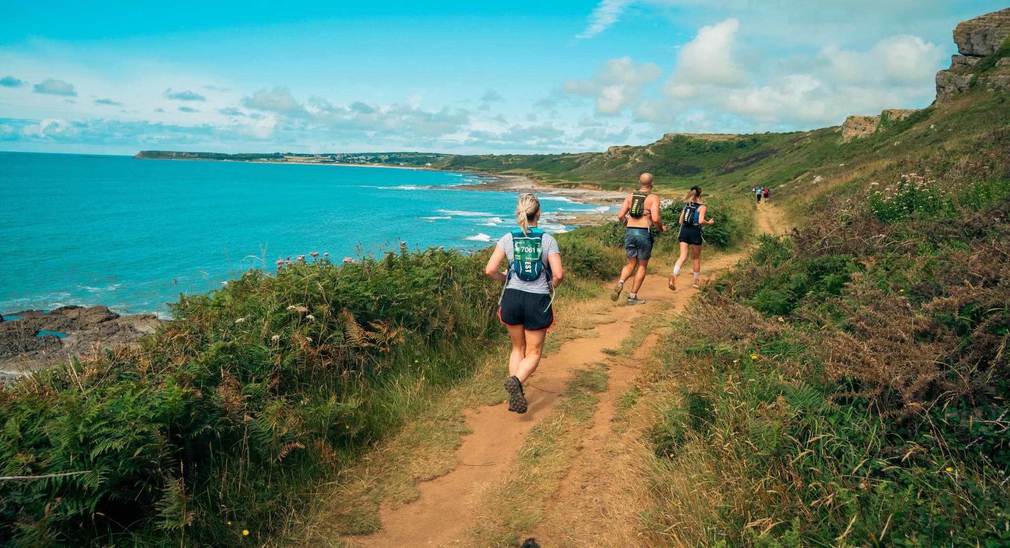 Runners running along the coastal path in the Gower, with the sea to the left.